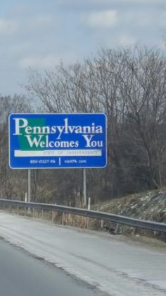 a blue sign that says pennsylvania welcomes you on the side of a road with trees in the background