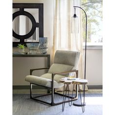 a chair and table in front of a window with a large circular mirror on the wall