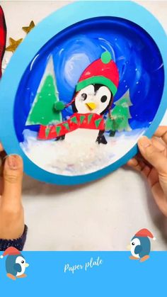 two hands are holding a paper plate with a penguin on it and a christmas tree