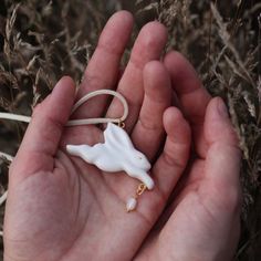 a hand holding a small white piece of jewelry in it's left palm area