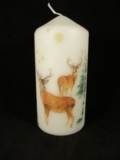 a white candle with deer on it and pine trees around the candlestick is shown in front of a black background