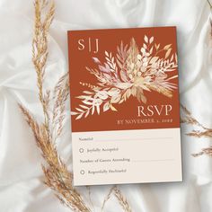 an orange and white wedding rsp card sitting on top of a bed with dried grass