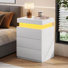 a white night stand with two drawers and a yellow strip on the bottom, in front of a bed