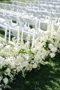 rows of white chairs lined up with flowers and greenery on the grass for an outdoor ceremony