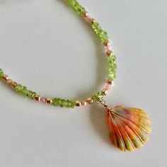 Hawaiian Sunrise Shell Necklace~ This necklace has a beautiful orange, pink, green wire wrapped Hawaiian sunrise shell with small pink faceted opals, green peridot chip gemstones and gold beads for accent. Sunrise shells are only found in Hawaii, a true gem to the islands and collectors.  Shell approx. .75" Necklace is adjustable 16- 18" Model wearing similar necklaces Checkout our sunrise shell jewelry~ https://www.etsy.com/shop/HanaMauiCreations?ref=seller-platform-mcnav&search_query=sunrise+shell+jewelry SHOP~  http://www.etsy.com/shop/HanaMauiCreations?ref=si_shop International buyers please read our shipping policies before ordering~ POLICIES~ https://www.etsy.com/shop/HanaMauiCreations/policy?ref=shopinfo_policies_leftnav Surfer Girl Gifts, Sunrise Shell, Tahitian Pearl Necklace, Necklace Gold Chain, Crystal Point Necklace, Black Pearl Necklace, Hawaii Beach, Peridot Gemstone, Green Peridot