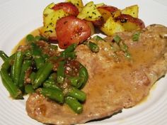 a white plate topped with meat and veggies next to potatoes on top of it