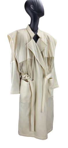 Rare and striking vintage coat from Jean-Charles de Castelbajac's Fall/Winter 1989-1990 Ready-to-Wear collection. Made from wool in a soft beige hue, the coat features an attached stringed waistcoat that cinches at the waist with a matching belt. The string detailing extends to the sleeves.  Two large front pockets provide practicality, while the bold, structured shoulder pads (removable if preferred) offer a strong silhouette distinctly of the era.  It falls just below the knee. Made in France Vintage Shawl Collar Outerwear For Fall, Vintage Winter Outerwear With Shawl Collar, Vintage Shawl Collar Winter Outerwear, Runway Ready To Wear, Structured Shoulder, Womens Jackets, Soft Beige, Vintage Coat, Shoulder Pads