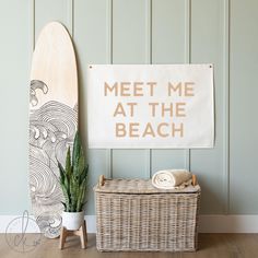 a surfboard next to a basket with towels on it and a sign that says meet me at the beach