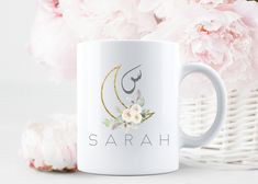 a white coffee mug sitting next to pink flowers