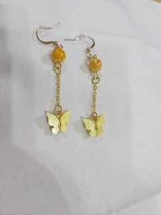 Yellow butterfly hanging from a gold colored chain with a yellow accent bead Gold Plated Beaded Dangle Jewelry, Gold Plated Dangle Jewelry With Beaded Chain, Trendy Gold Earrings With Dangling Beads, Gold Metal Earrings With Butterfly Charm, Gold Earrings With Butterfly Charm, Gold Dangle Earrings With Beaded Chain, Trendy Gold Beaded Earrings With Dangling Beads, Trendy Dangle Gold Chain Jewelry, Trendy Gold Jewelry With Dangling Beads