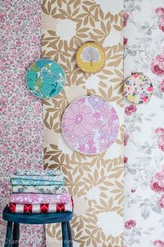 wallpaper with flowers and plates on it next to a stool in front of a flowered wall