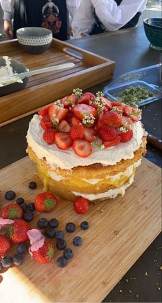 a cake with strawberries and blueberries on it sitting on top of a wooden cutting board