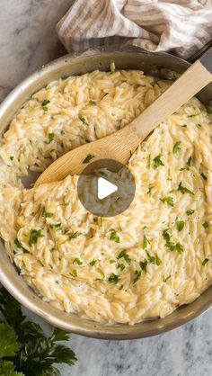 a pot filled with pasta and parsley on top of a marble counter next to a wooden spoon