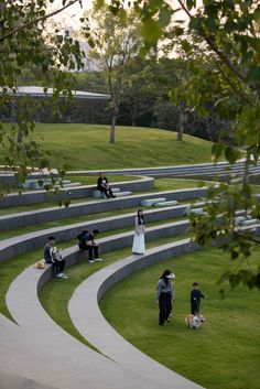 several people are sitting on the grass near some stairs and benches with trees in the background