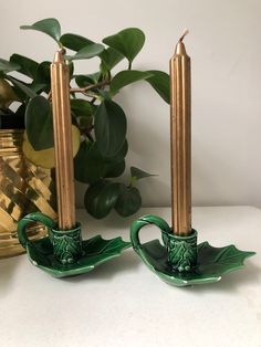 two green candlesticks sitting on top of a table next to a potted plant