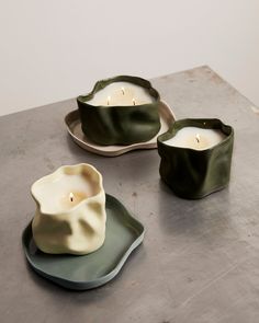 two green and white dishes with candles in them on top of a gray tablecloth