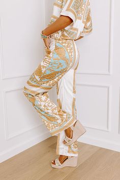 - Step into the spotlight with these fabulous satin-finished pants! Its charming relaxed fit is both trendy and classy, while the ornate print adds a dash of elegance and fun. Perfect for any occasion, this piece is your new go-to for effortlessly chic energy. - Fully lined material with an ornate print featuring mustard, blue, and neutral hues and satin finish - Side zip closure - Functional side pockets - A relaxed silhouette that ends in straight hemlines Measurements S : Front Rise 12.5", Hi Elegant White Printed Bottoms, Elegant Wide Leg Printed Pants, White Satin Bottoms For Summer, Elegant Printed Wide-leg Pants, Chic White Printed Bottoms, Beige Satin Bottoms For Spring, Gold Chic Sets For Spring, Chic Gold Sets For Spring, Elegant Printed Summer Pants