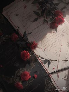 an open book with red roses on it next to a pair of scissors and some writing paper