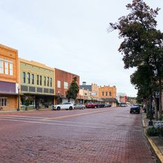 an empty street with cars parked on both sides and buildings in the backround