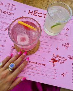 a woman's hand on top of a pink menu with a drink and ice cubes