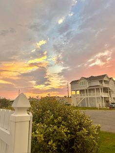 a white picket fence sitting next to a lush green field under a cloudy sky at sunset