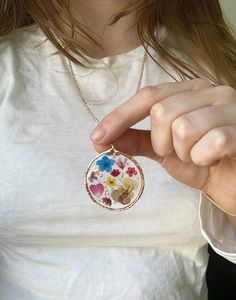 Oh wildflowers 🌸 is there anything better? This big circular pendant is made of real pressed flowers preserved into resin. There is gold leafing sprinkled into the resin to make the pendant really sparkle ✨This is made to last a long time and the high quality resin preserves the flowers to stay at this vibrancy for as long as the necklace lasts! The pendant is on a super long 28 inch chain with NO clasp. You can easily slip this over your head without having to mess with the closure in the back Bohemian Jewelry With Pressed Flowers In Resin, Gold Flower Necklace With Pressed Flowers In Round Pendant, Bohemian Gold Resin Necklace, Resin Round Pendant With Flower Charm, Botanical Style Gold Resin Jewelry, Resin Necklace With Pressed Flower Pendant, Resin Necklace With Pressed Flowers In Round Pendant, Resin Birth Flower Necklaces For Jewelry Making, Resin Birth Flower Pendant Necklace