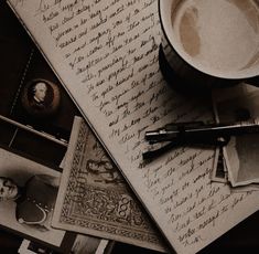 a cup of coffee sitting on top of an open book next to a pen and paper