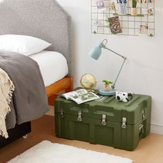 a green suitcase sitting on top of a wooden floor next to a lamp and bed