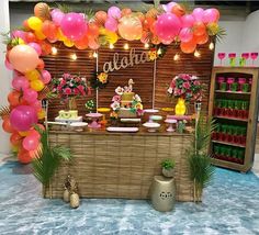 a table topped with lots of pink and orange balloons next to a shelf filled with bottles