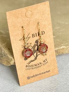 Czech glass coins in a shiny, vibrant burgundy red and etched in a wild rose shape. These nature-inspired glass dangle earrings are perfect for dressing up or down, adding a boho shimmer to vintage-inspired styles. Welcome to our Bohemian-inspired earring collection, where free-spirited fashion meets timeless elegance. Each pair of earrings is meticulously crafted with exquisite Czech glass floral beads, offering a touch of bohemian charm to any ensemble.Embrace individuality with our diverse ra Czech Glass Earrings As A Gift, Vintage Czech Glass Flower Earrings Gift, Vintage Czech Glass Flower Earrings For Gift, Red Round Jewelry With Flower Charm, Red Bohemian Jewelry With Flower Charm, Red Czech Glass Jewelry, Red Pressed Flowers Earrings For Gift, Flower Charm Earrings With Czech Glass As Gift, Vintage Red Flower Earrings For Gift