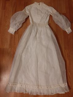 an old white dress is laying on the floor with wood floors in front of it