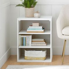 a white shelf with books and plants on it in a room next to a chair