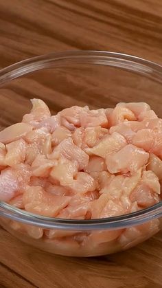 a glass bowl filled with raw chicken on top of a wooden table