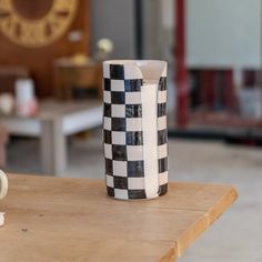 a black and white checkered vase sitting on top of a wooden table next to a coffee cup