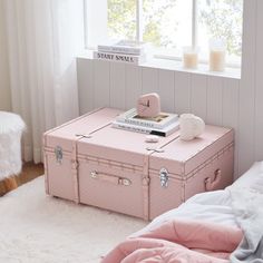 a pink suitcase sitting on top of a bed next to a white rug and window