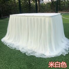 a white table covered in tulle on top of a green field with trees behind it