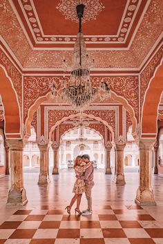 two people standing in an ornate building with chandelier and red tile flooring