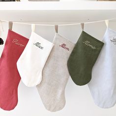 three stockings hanging from a clothes line with personalized names on them and pine cones in the background