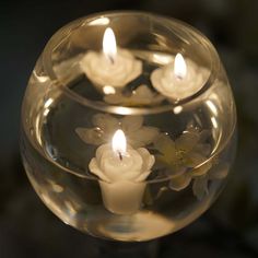 three lit candles in a glass bowl filled with water and floating flowers on the bottom