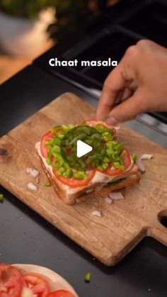 a person is making a sandwich on a cutting board with tomatoes and green onions in the middle