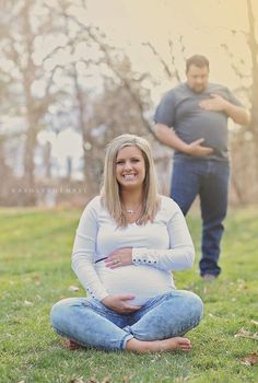 a pregnant woman sitting on the ground in front of a man with his arm around her belly