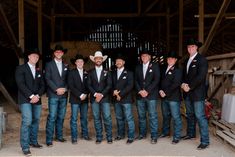 a group of men standing next to each other in front of a wooden structure wearing cowboy hats