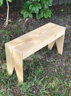 a wooden bench sitting on top of a grass covered field next to a tree and bushes