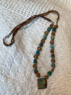 Embrace the beauty of nature with this handcrafted leather necklace, featuring a stunning turquoise pendants. The earthy tones of wood jasper and the vibrant blue-green of turquoise beads create a harmonious blend, while the soft leather cord adds a touch of rustic elegance. Perfect for any occasion, this unique piece is sure to be a conversation starter and a cherished addition to your jewelry collection. Bohemian Brown Jasper Beaded Necklaces, Bohemian Brown Leather Necklace, Earthy Turquoise Necklace With Natural Stones, Artisan Beaded Brown Turquoise Necklace, Artisan Brown Beaded Turquoise Necklace, Artisan Brown Turquoise Necklace With Gemstone Beads, Bohemian Brown Turquoise Necklace With Gemstone Beads, Bohemian Adjustable Turquoise Necklace With Wooden Beads, Adjustable Brown Turquoise Bohemian Necklace