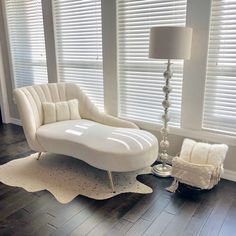 a white chair and lamp in a room with windows covered in blinds on the side