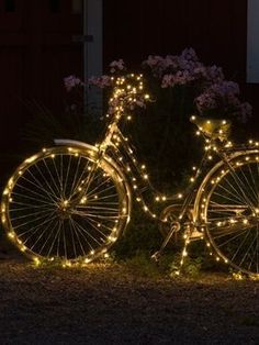 a bicycle is decorated with fairy lights in front of some flowers and bushes at night