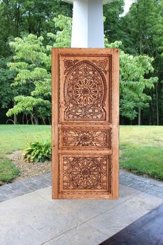 an intricately carved wooden panel on display in front of a building with trees and grass behind it