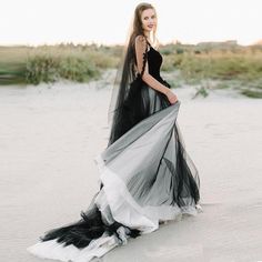 a woman standing on top of a sandy beach wearing a black and white wedding dress