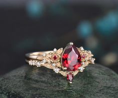 Introducing our Vintage Pear Red Ruby Engagement Ring set, a masterpiece inspired by the allure of nature's intricate beauty. This unique cluster diamond bridal wedding ring set seamlessly blends vintage charm with modern elegance. Ring set comes with the engagement ring and band. By default, the accent stones are set with moissanite accents from VS to VSS clarity. Please contact us if you would like to have this changed to lab grown or natural diamonds. Product Details Pear Red Ruby: The heart Ruby Ring Vintage Red Antique Jewelry, Ruby And Gold Engagement Ring, Red Rings Engagement, Ruby And Gold Ring, Red And Gold Ring, Opal And Ruby Ring, Engagement Rings With Ruby, Diamond And Ruby Engagement Rings, Wedding Rings Ruby