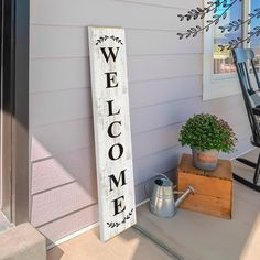 a welcome sign sitting on the front porch next to a chair and potted plant